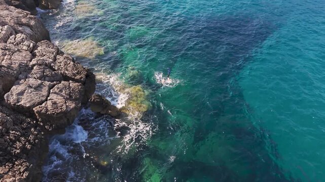 Aerial View of Freediver Diving Through Turquoise Water Beside Limestone Cliffs at Voidokilia, Greece