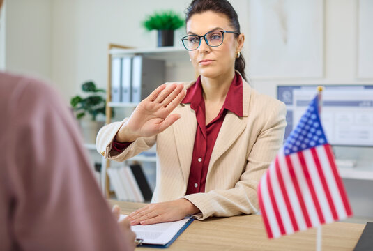 Consultant and client face visa interview rejection. Adviser signals refusal as documents rest on desk. American flag and monitor show USA office. Clear sign of immigration rejection concept.