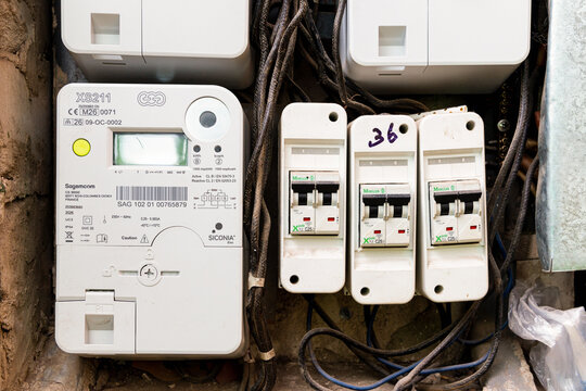 Old digital electric meter and circuit breaker mounted on a weathered industrial panel with rusty metal structures, showing energy usage measurement and vintage wiring. Telsiai, Lithuania 08-26-2026