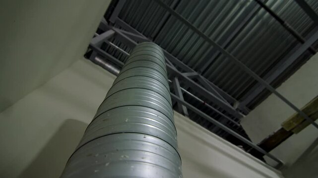 Industrial air duct pipe rises vertically in high-ceiling commercial facility space. HVAC engineering installation ensures climate control