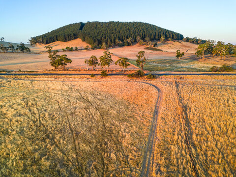 Aerial view of dry paddocks and a country road in front of a mountain covered in trees