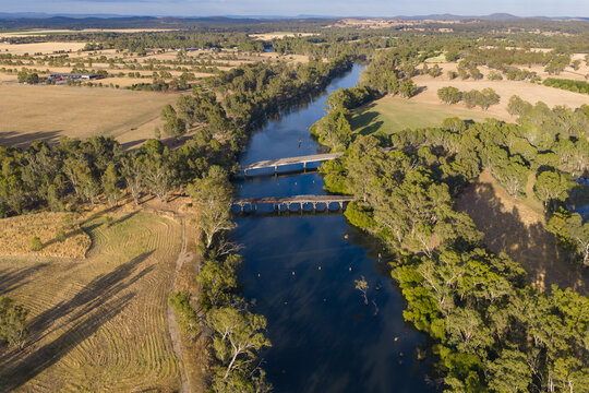 Aerial view of twin bridges across a wide running through dry countryside