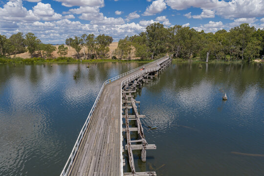 Aerial view over a abandoned wooden bridge over a calm river with cloud reflections