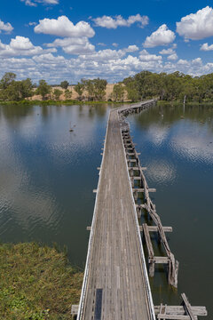 Aerial view over an abandoned wooden bridge over a calm river with cloud reflections