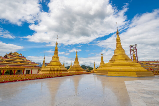 Pyay Tha Lin Aye Pagoda, known as Phra That Tagaw, features beautiful golden stupas of various sizes standing on a wide open courtyard under a bright blue cloudy sky in Kayin State, Myanmar.
