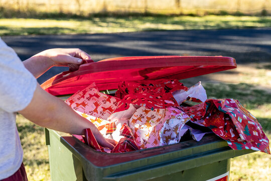 Person disposing festive wrapping paper into outdoor garbage bin after celebrations