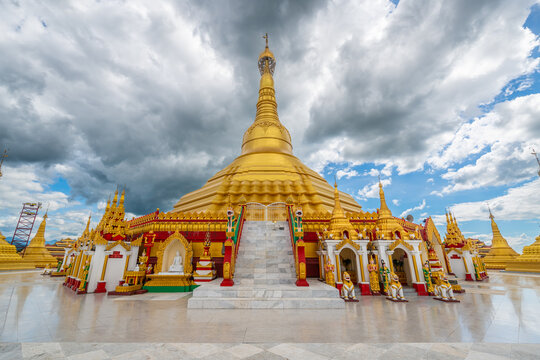 Pyay Tha Lin Aye Pagoda, known as Phra That Tagaw, features stairs leading up to a golden stupa surrounded by small shrines under a dramatic cloudy sky in Kayin State, Myanmar.