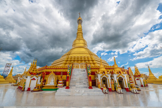 Pyay Tha Lin Aye Pagoda, known as Phra That Tagaw, features stairs leading up to a golden stupa surrounded by small shrines under a dramatic cloudy sky in Kayin State, Myanmar.