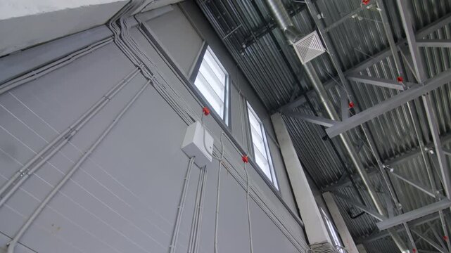 Square air diffusers connected to shiny metal ductwork overhead. Wall paneling integrates organized wiring conduits under roof structure