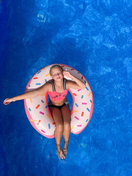 Top view of a happy blonde little girl floating in a swimming pool on an inflatable donut swim ring with her eyes closed