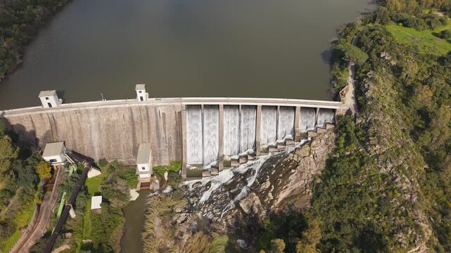 Water Flowing Over The Concrete Spillway Of Lago Di Monte Pranu Dam In Sardinia, Italy. aerial pullback, tilt-up shot