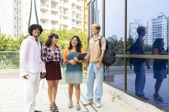 Diverse group of indian gen z college students enjoy conversing outdoors on campus, holding notebooks and wearing backpacks, representing education, friendship, and learning together