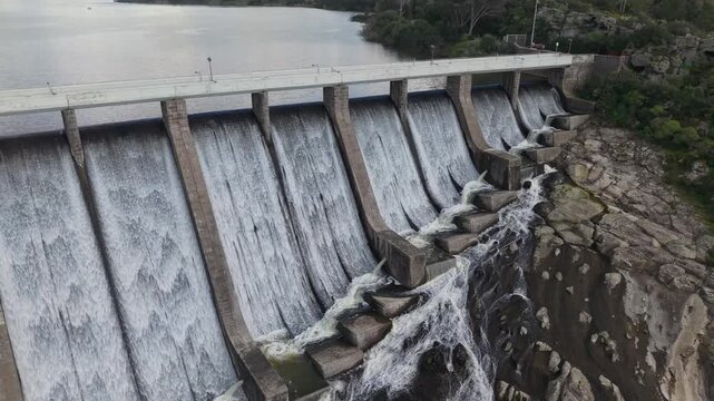 Lateral View Of Diga di Monte Pranu In Sardinia, Italy With Water Overflowing Through Spillways. drone pullback shot
