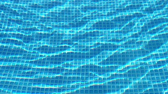Full-frame shot of sunlight refracting through rippling water onto a blue grid-patterned pool bottom. Ideal for summer advertising, resort promos, and pool maintenance.