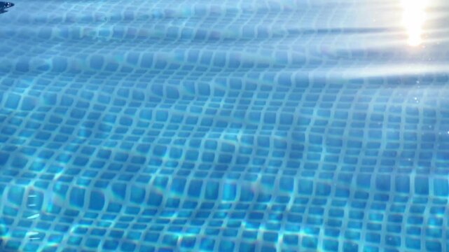 Angle shot of bright sunlight reflecting off rippling blue water in a tiled swimming pool. Ideal for summer travel campaigns, resort promo videos, and pool cleaning ads.