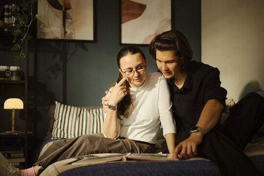 Young diverse couple sitting on bed and looking at photo album together, remembering memories. Image suitable for family lifestyle and relationship counseling marketing