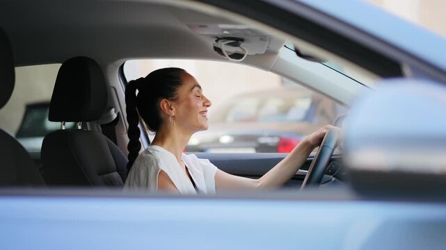 Young cheerful Hispanic woman talking on a hands-free phone call through the car&rsquo;s Bluetooth system while sitting in the driver&rsquo;s seat of a parked car