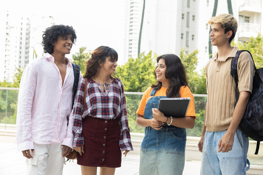 Diverse group of indian gen z college students enjoy conversing outdoors on campus, holding notebooks and wearing backpacks, representing education, friendship, and learning together