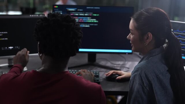Diverse software developer team coding on computer monitors. Smiling Asian female programmer discussing IT projects with African American colleague. Corporate technology, and modern teamwork concepts