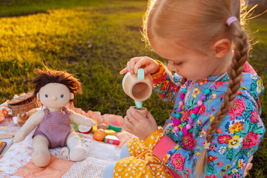 young child playing picnic outdoors in backyard with tea set at sunset