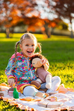 happy girl playing with wooden tea set toys and doll outdoors having a pretend picnic