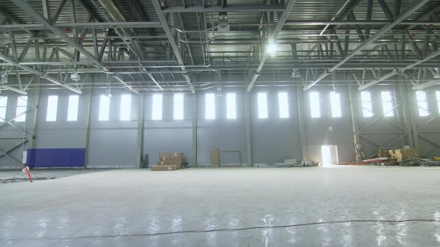 Doorway opening leads view into industrial hall with steel roof structure. Light reflects on concrete floor of new building project