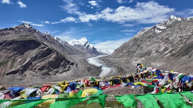 Zanskar, India : Titl down slow motion footage of prayer flags blown by wind with Drang Drung glacier, long river ice in Zanskar valley of Ladakh, India in the background surrounded by rocky mountain 