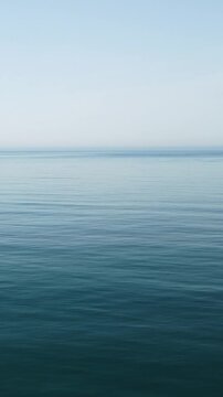 Vertical aerial view over calm azure sea water surface. Sun glare. Abstract nautical summer ocean nature. Holiday, vacation and travel concept. Nobody. Weather and climate change