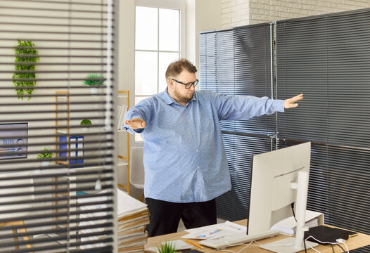 Man in office dancing near computer after success. Cheerful employee takes a quick break, celebration of results and easing stress in a busy workplace. Concept of workplace joy and achievement.