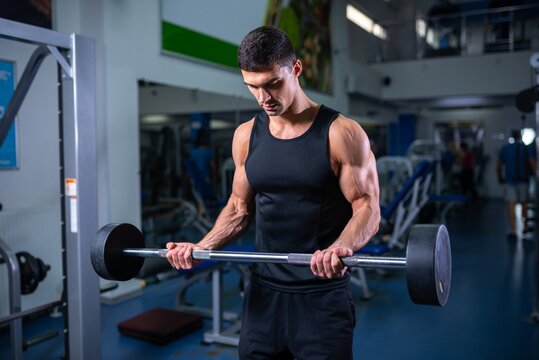 Focused bodybuilder doing a bicep curl with a straight barbell