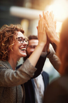 A group of three people celebrate a successful moment by giving high fives in a bright office. The sun shines through large windows