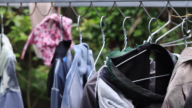 Row of clothes on wire hangers drying outdoors on a chain link fence in a rustic countryside backyard