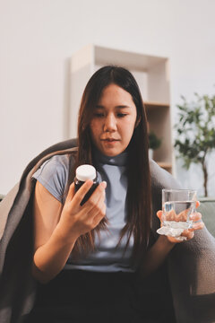 sick asian young woman sneezing into tissue paper while covered with a blanket and sitting on sofa in the living room