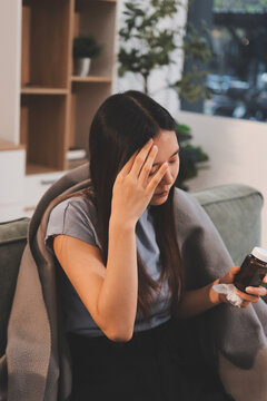 sick asian young woman sneezing into tissue paper while covered with a blanket and sitting on sofa in the living room