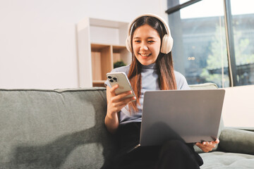 Beautiful young asian woman sitting on sofa and holding joystick playing online video game in living room at house © ARMMY PICCA