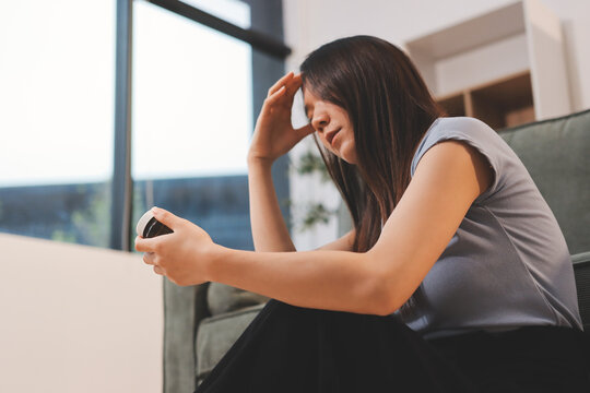 Young Asian woman sitting in bed and holding her head in pain with headache, feeling depressed 

and suffering