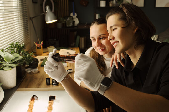 Young diverse couple examining analog film negatives on light table in home studio. Image represents creative hobby, photography education, and retro lifestyle marketing