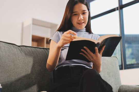 Freelance Asian woman holding mobile phone typing on laptop and working from home. Happy young girl sitting on sofa in living room.