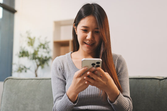 Happy relaxed young woman sitting on couch using cell phone, smiling lady laughing holding smartphone, looking at cellphone enjoying doing online ecommerce shopping in mobile apps or watching videos.