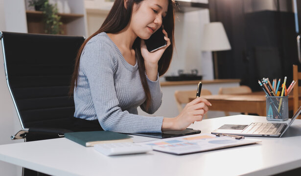 Young Asian woman sits at office desk rubbings her eyes and temples feeling pain. Stress. And exhaustion from long hours working on the computer