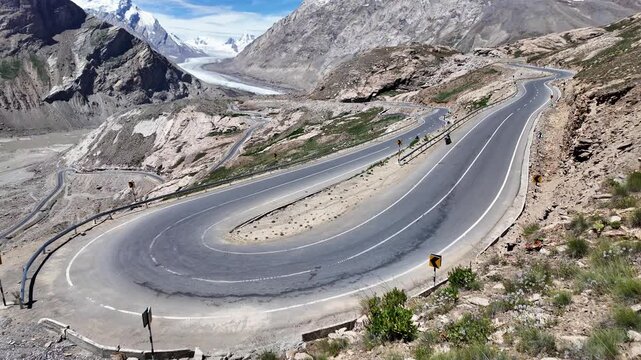 Zanskar, India : Tilt up mountain road in Pensi La, famous mountain pass in Zanskar of Ladakh, India with dramatic rocky mountain range and Drang drung glacier on sunny day in the background