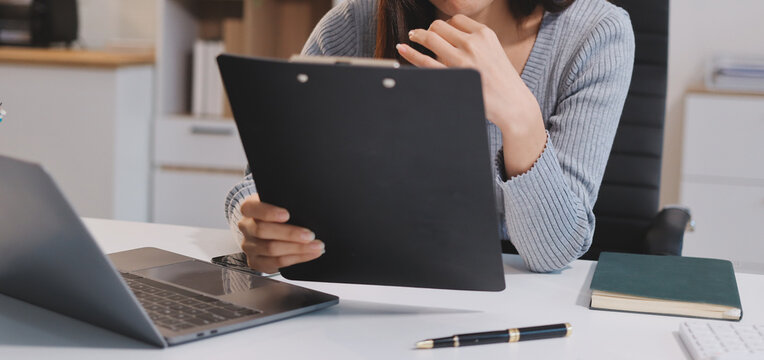 Young Asian woman sits at office desk rubbings her eyes and temples feeling pain. Stress. And exhaustion from long hours working on the computer
