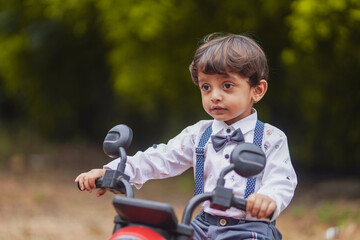 Fototapeta premium A cute Indian little boy in a stylish outfit enjoys riding a red