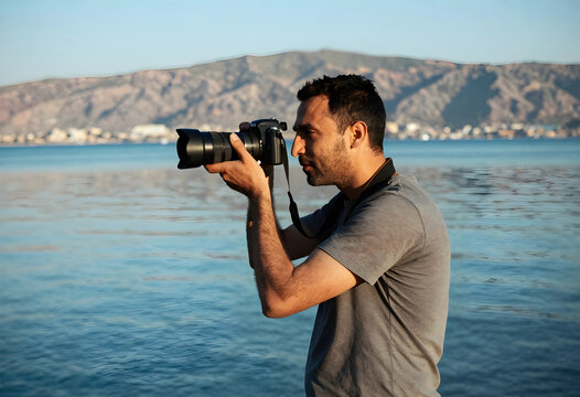 Photography hobby and creative lifestyle, man taking pictures with professional camera at the seaside during golden hour with mountain landscape background