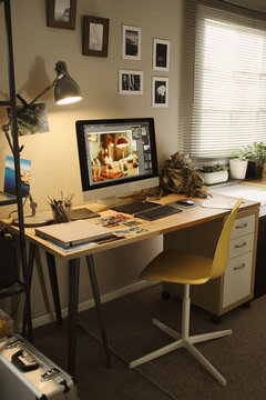 Vertical image of creative home office workspace featuring computer monitor displaying photo editing software. Scene represents remote work and digital design career marketing