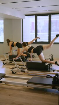 Women engage in a pilates session using reformer machines in a bright, modern studio. Group exercise class focusing on body strength and flexibility with specialized equipment.
