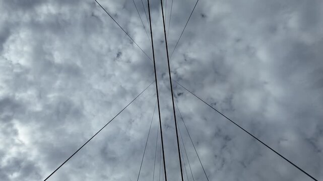 Steel cables of a suspension bridge stretch against cloudy sky.