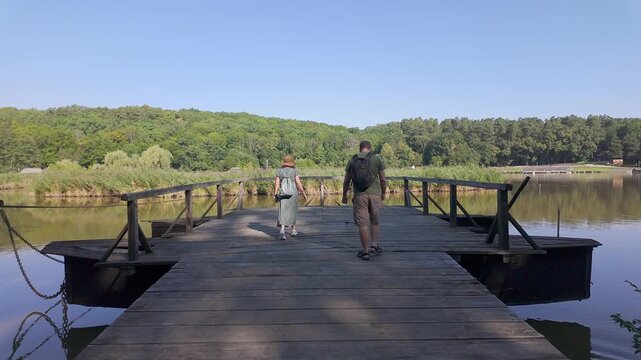 Two tourists walking on a wooden pier over a calm lake surrounded by forest in Romania