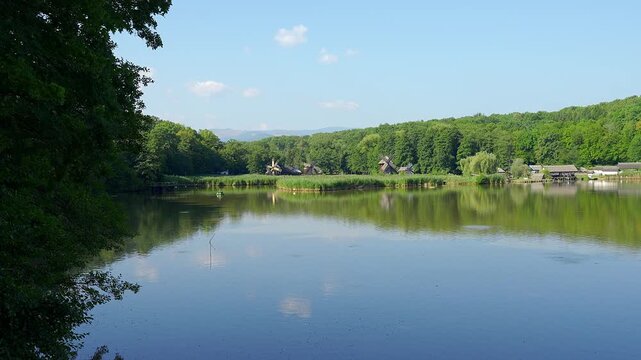 Scenic Romanian lake with traditional windmills forested hills and reflections under blue sky