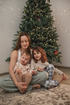 Mother and daughters opening presents under the tree, New Year and Christmas celebrations. Gift wrapping real people, real emotions